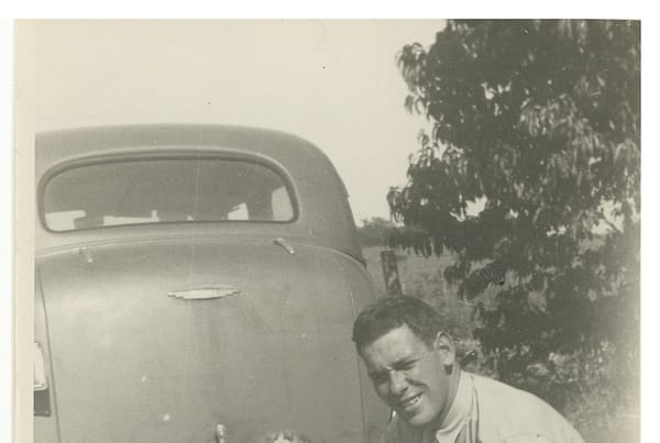 A man kneeling down next to a child in front of an old car.