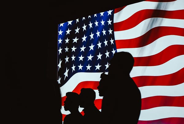 A man and woman standing in front of an american flag.