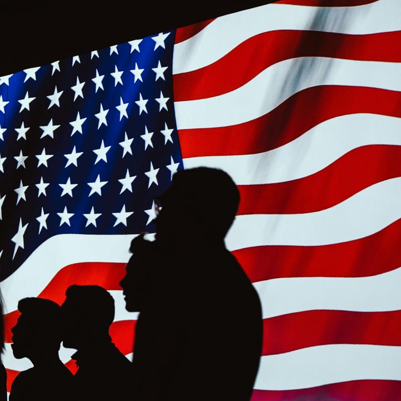 A man and woman standing in front of an american flag.